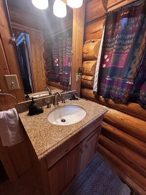 A wooden cabin bathroom with a granite countertop sink, a mirror, and a towel hanging on the wall. - Lamar Valley Mountain Cabin (Silver Gate)