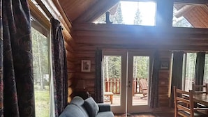 A cozy log cabin interior with a sofa, dining table, and large windows. - Lamar Valley Mountain Cabin (Silver Gate)