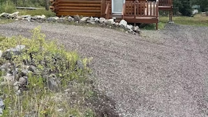 A log cabin with a porch and a door, surrounded by a forest and a mountain in the background. - Lamar Valley Mountain Cabin (Silver Gate)
