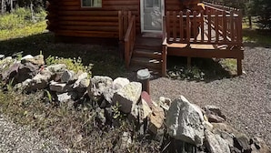 A log cabin with a wooden porch and a stone wall in front. - Lamar Valley Mountain Cabin (Silver Gate)