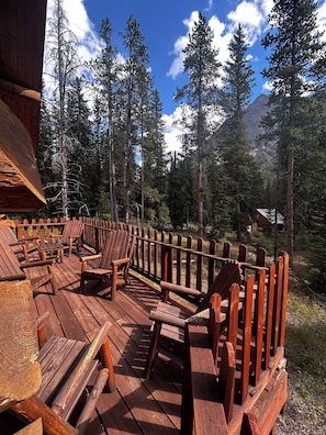 Une terrasse en bois, agrémentée de chaises Adirondack et entourée d’une balustrade en bois, qui offre une vue sur une zone montagneuse boisée.