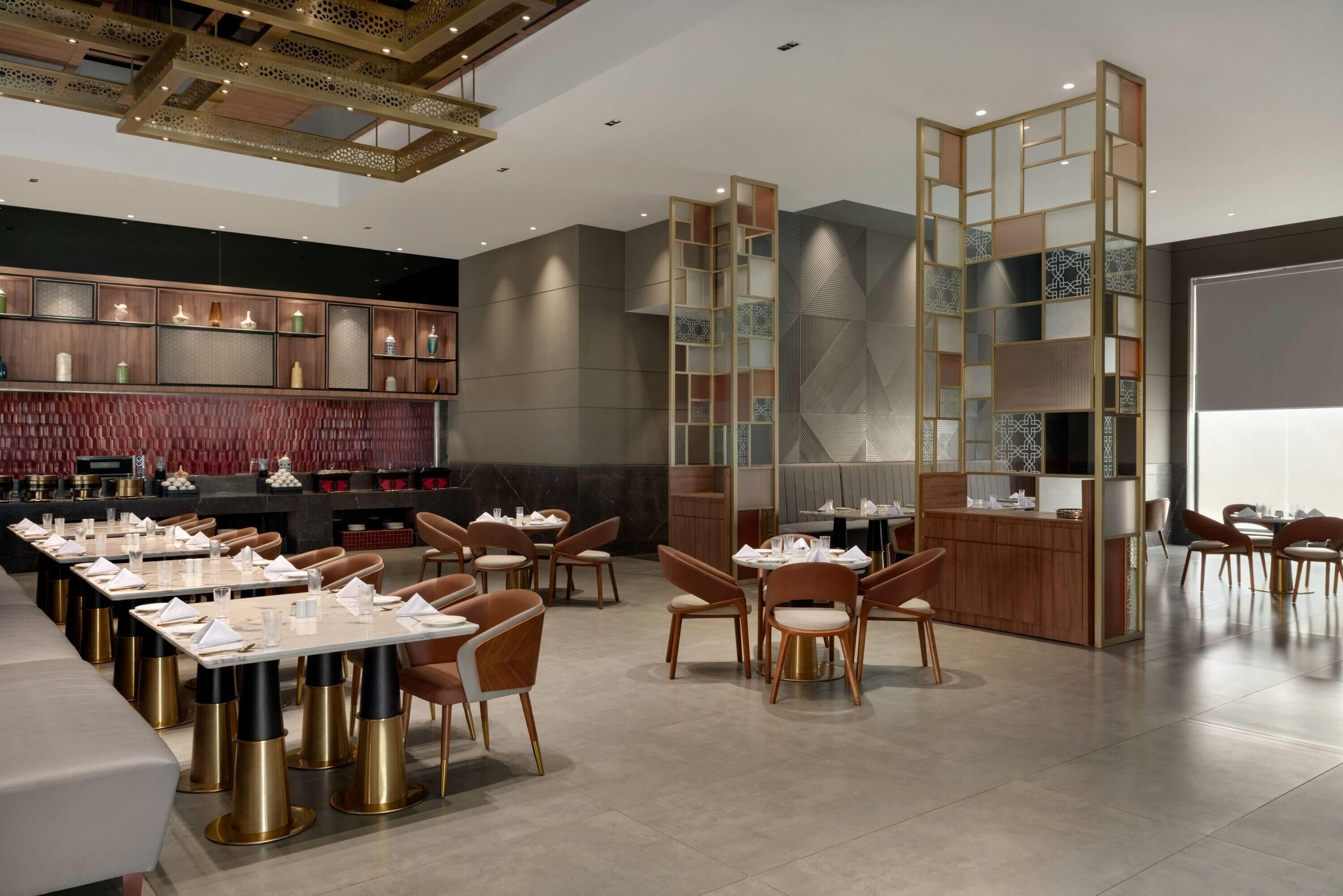 A modern restaurant with a long dining table, multiple chairs, and a decorative wall with shelves.