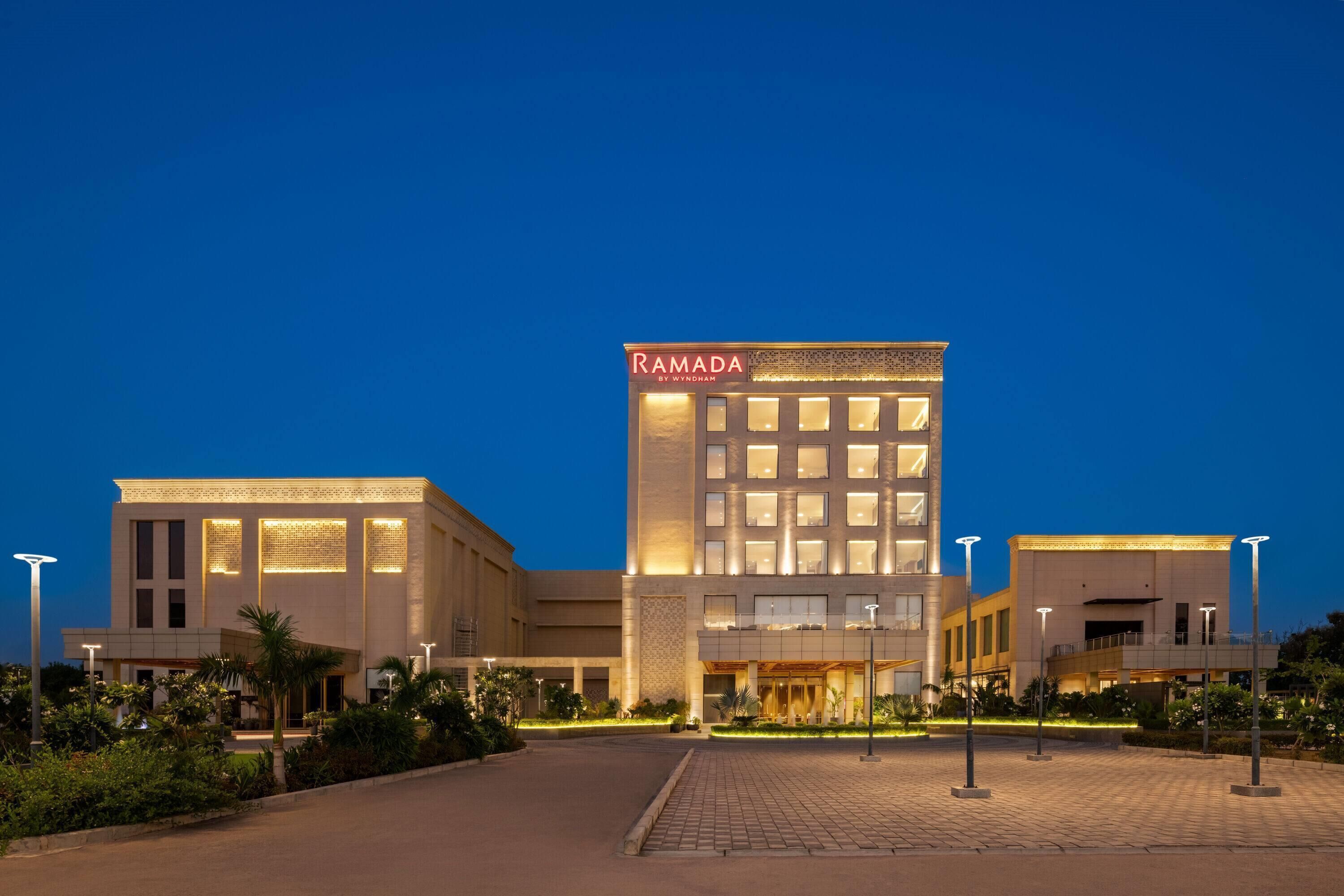 A modern hotel with a prominent "Ramada" sign, featuring a central entrance, multiple floors, and a well-lit facade.