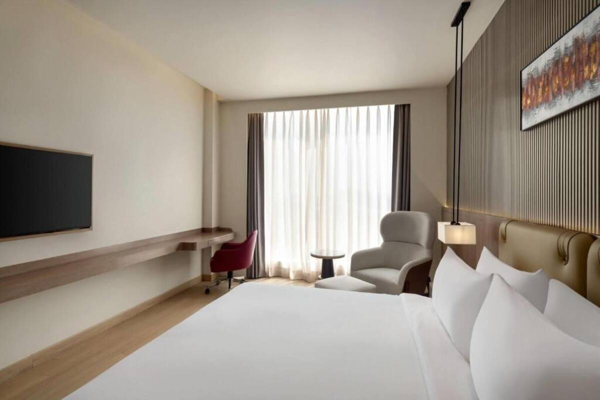 A hotel room with a large bed, a desk, a chair, a TV, and a window with curtains.