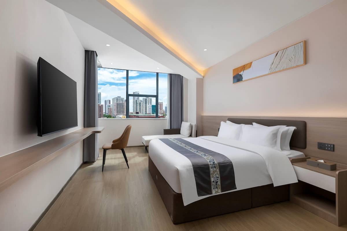 A modern hotel room with a large bed, a flat-screen TV mounted on the wall, a desk, and a chair.