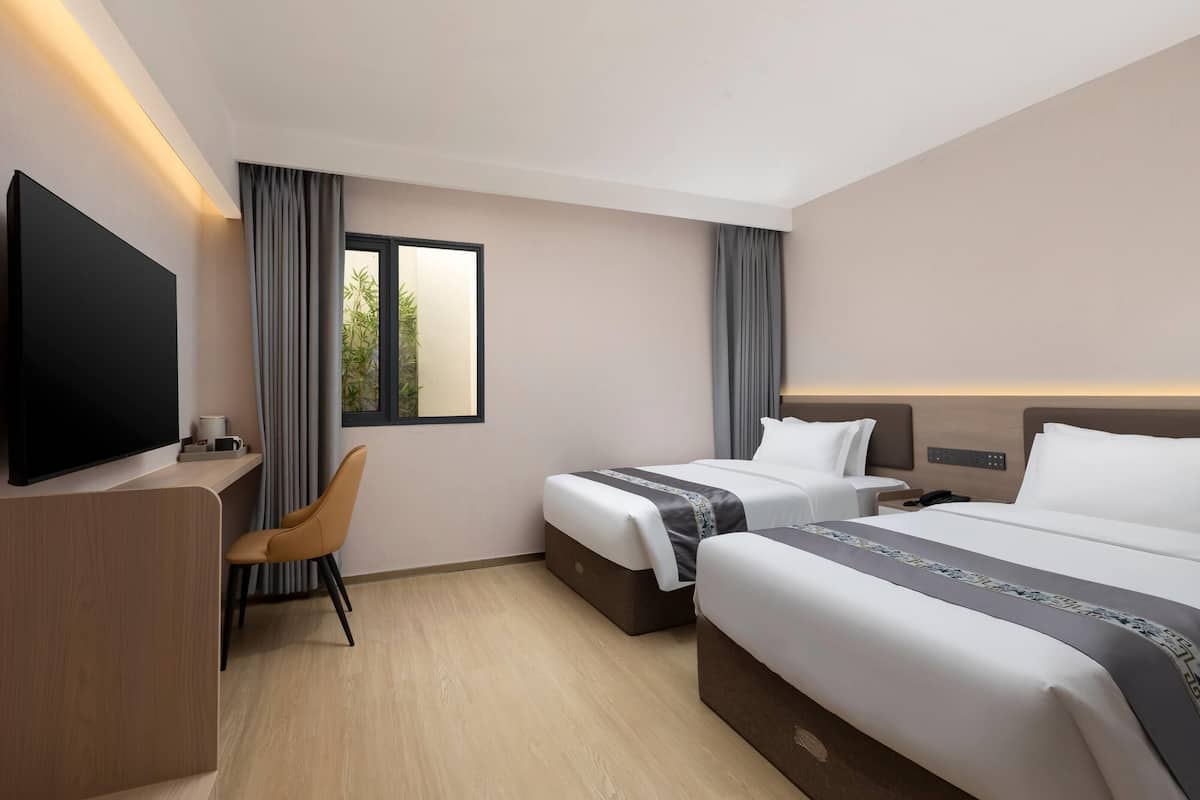 A hotel room with two beds, a desk, a chair, a TV, and a window with curtains.