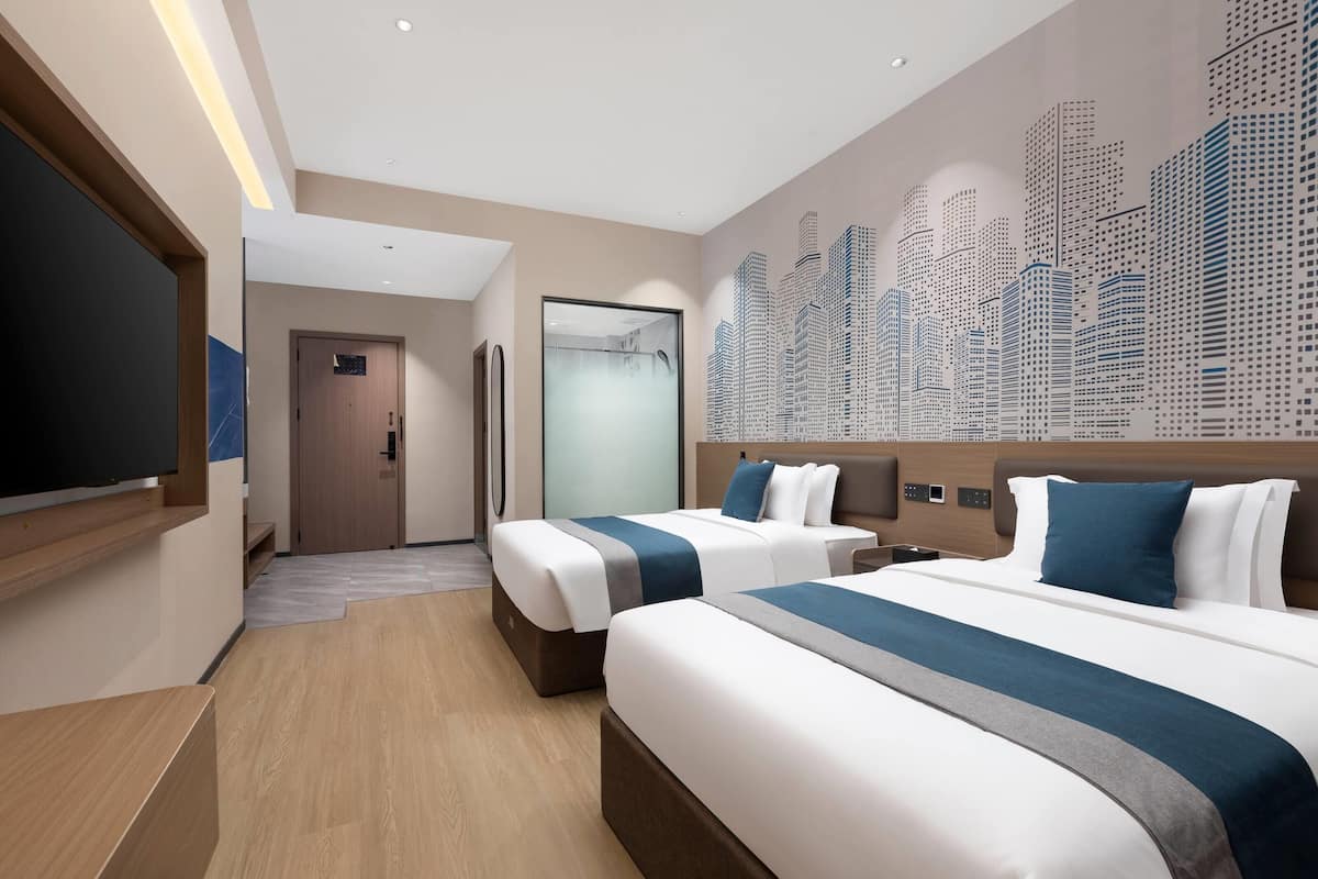 A hotel room with two beds, a television, a cityscape mural, and a wooden floor.