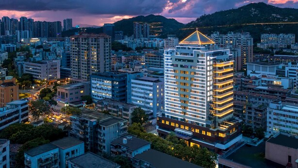 A high-rise building with a distinctive triangular roof, surrounded by other residential and commercial buildings. - Days Inn by Wyndham Zhuhai Qinglv Road (Zhuhai)