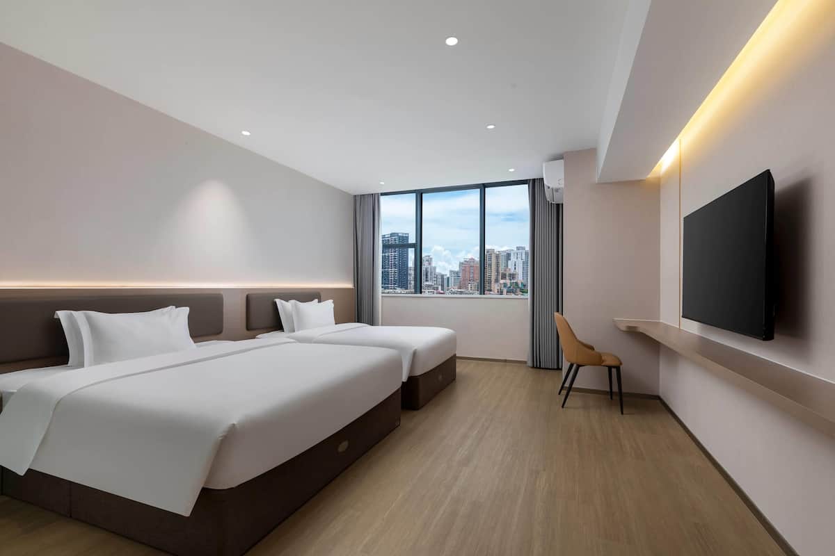 A modern hotel room with two beds, a TV, and a city view.