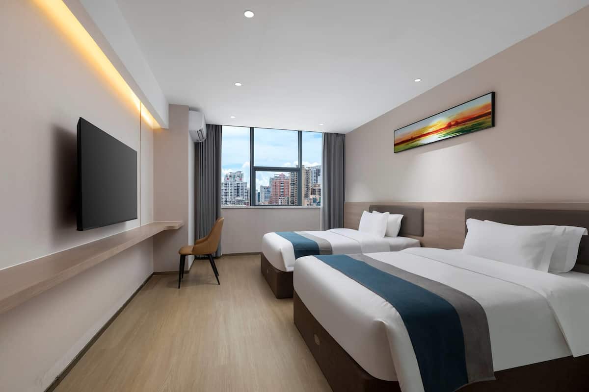 A hotel room with two beds, a TV, a city view, and a painting on the wall.