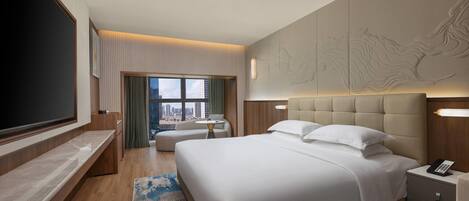 A modern hotel room with a large bed, a flat-screen TV, a desk, and a view of the city.