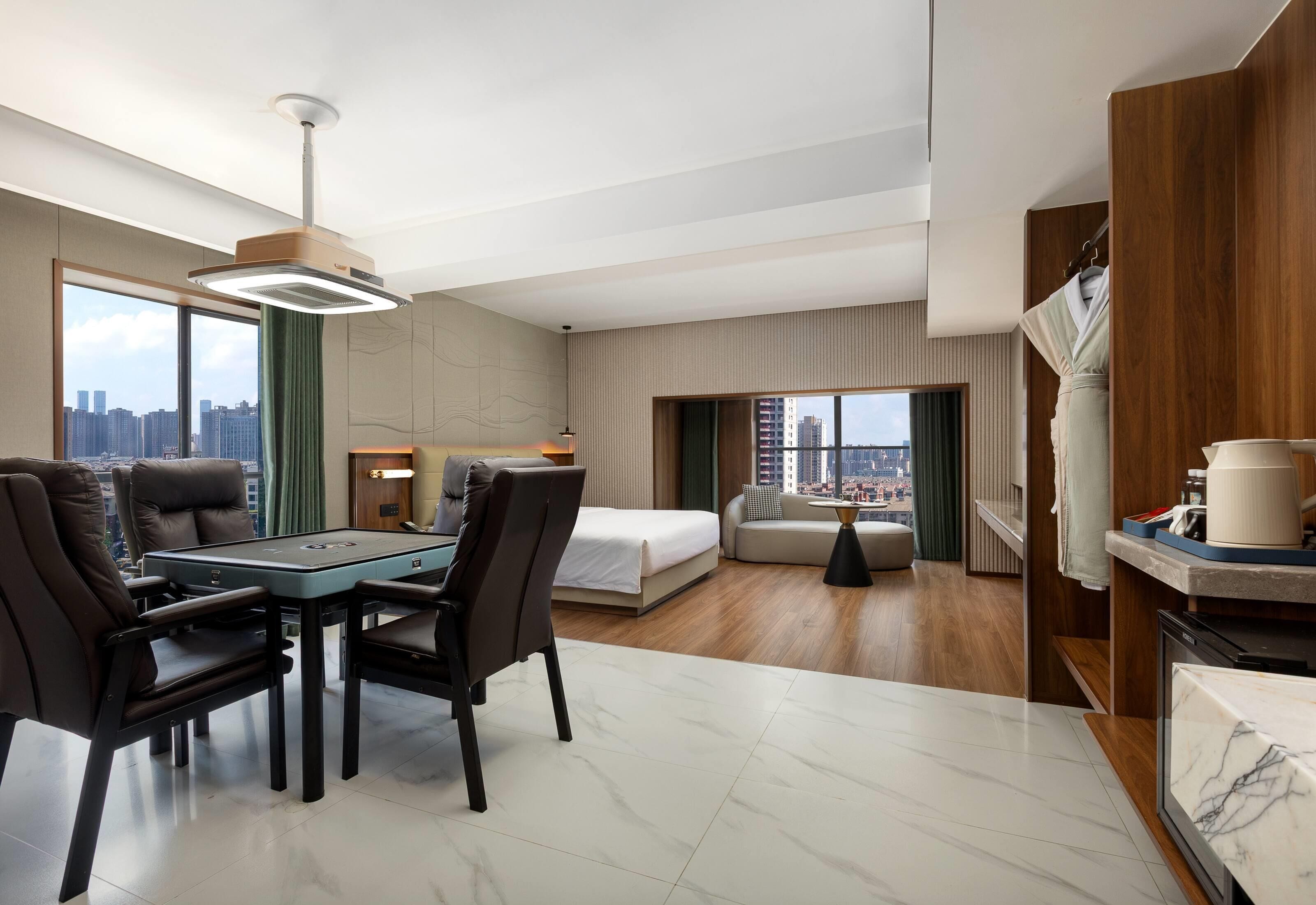 A modern hotel room with a dining area, a bed, a sofa, and a view of the city skyline.