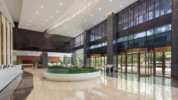 A spacious lobby with a central water feature, large windows, and a modern reception desk. - Ramada Encore By Wyndham Enshi Huaxi Valley (Enshi)