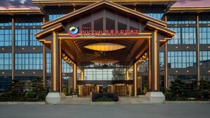 A modern hotel entrance with a covered lobby, large windows, and a prominent sign. - Ramada Encore By Wyndham Enshi Huaxi Valley (Enshi)