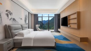 A modern hotel room with a large bed, a flat-screen TV, a desk, and a chair. - Ramada Encore By Wyndham Enshi Huaxi Valley (Enshi)