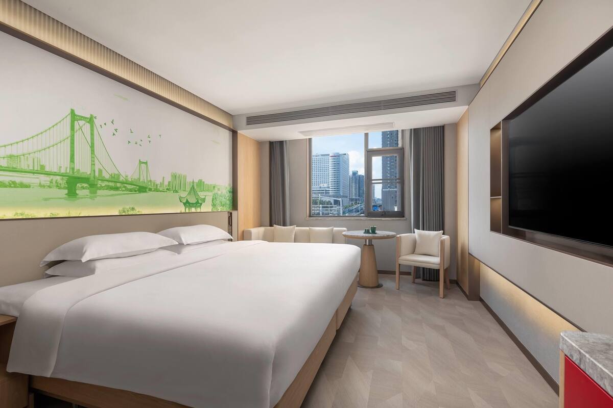 A hotel room with a large bed, a desk, a chair, a TV, and a mural of a bridge.