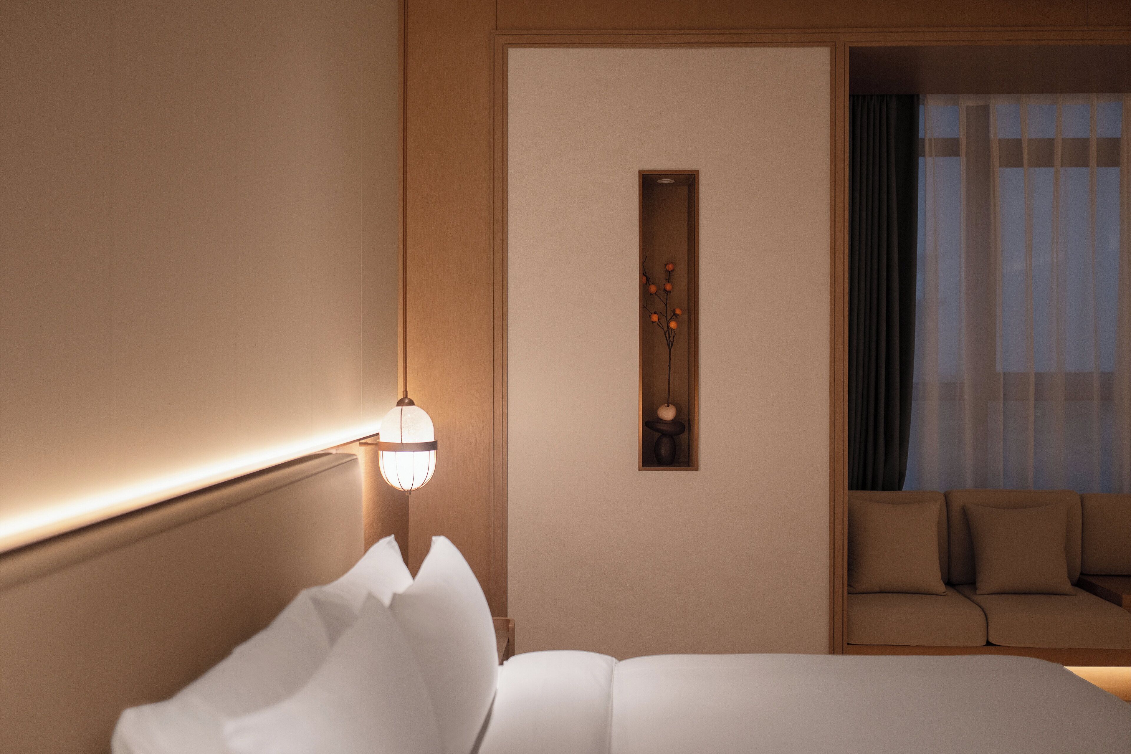 Une chambre d’hôtel avec un lit, un canapé, une lampe fixée au mur et une petite étagère décorative.