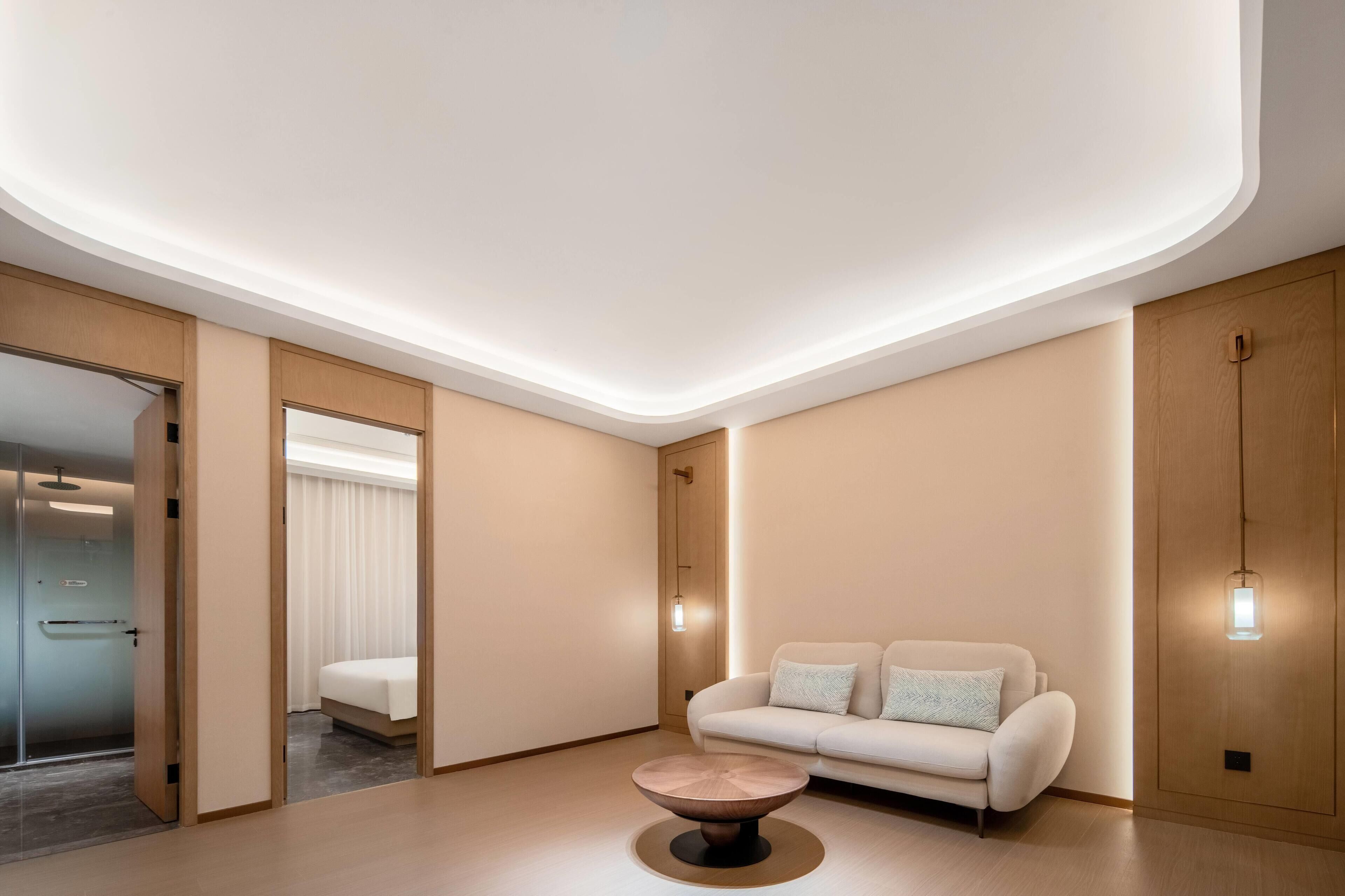 Een moderne hotelkamer met een minimalistisch design, met een bank, een ronde salontafel en een grote spiegel.