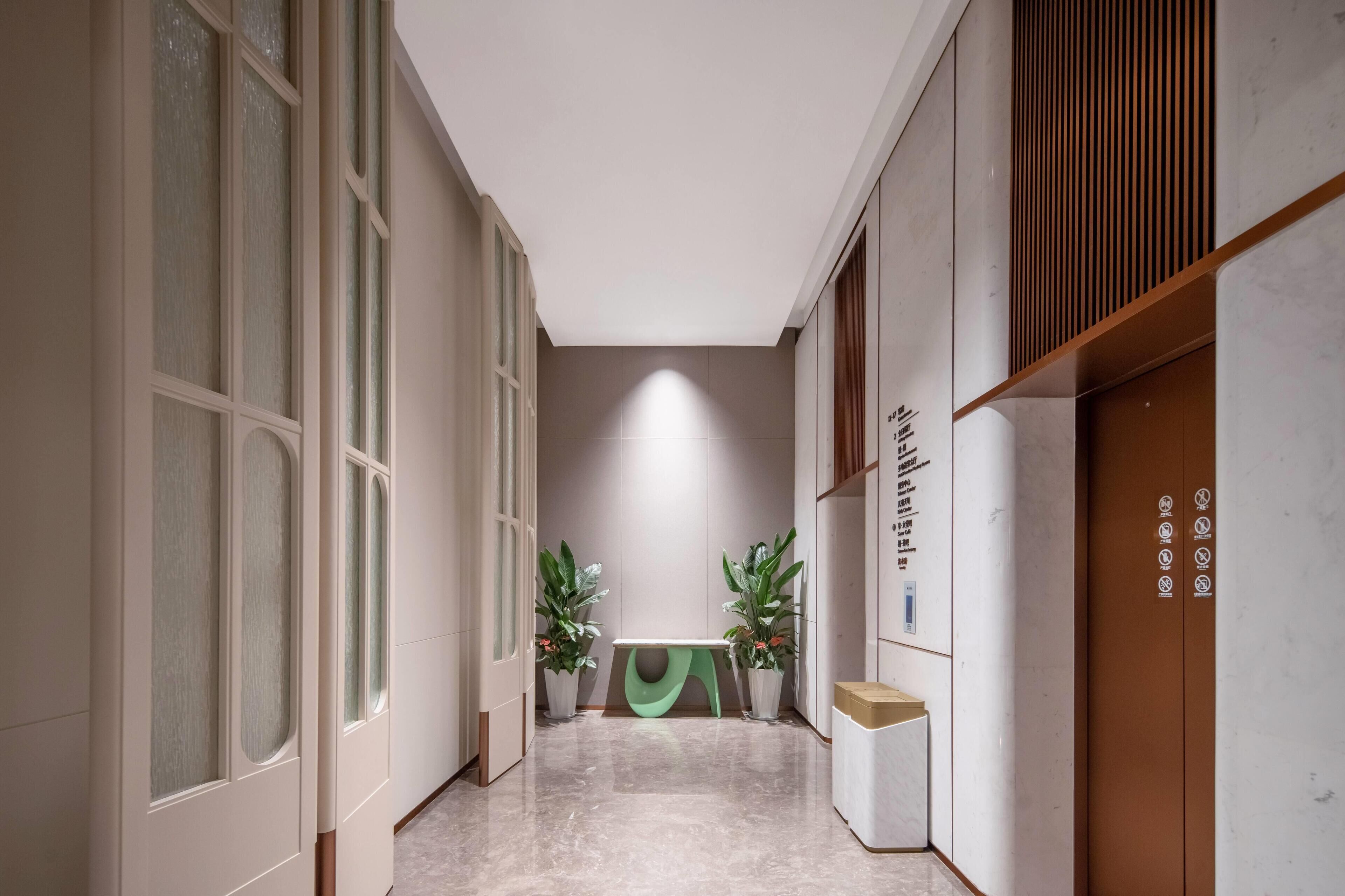 A hallway with a bench, potted plants, and a door with symbols.