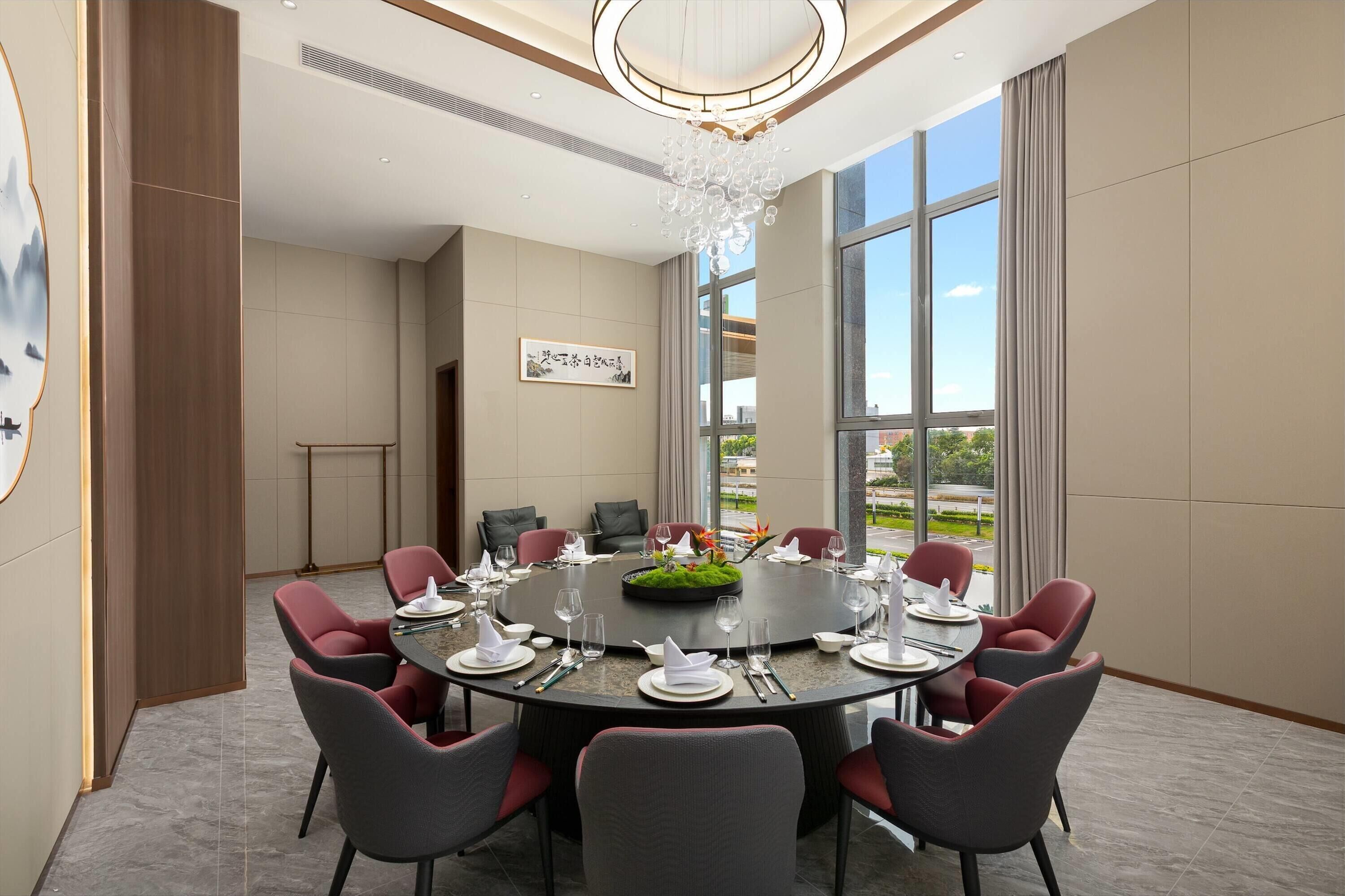 A modern conference room with a round table, red and grey chairs, and a chandelier.