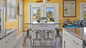 A kitchen with a central island, bar stools, a hanging light fixture, and a framed map on the wall. - The Gulf Breeze - Direct Access To Gulf (Hernando Beach)