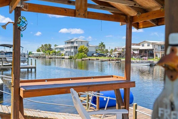 A wooden dock with a bench, a blue lounge chair, and a view of houses and water.