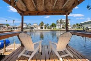 Une terrasse en bois avec deux chaises Adirondack blanches, donnant sur une étendue d’eau calme, et en arrière-plan, on aperçoit des immeubles résidentiels.