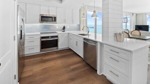 A modern kitchen with white cabinetry, stainless steel appliances, and a wooden floor.