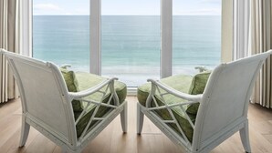 A room with two white wicker chairs facing a large window overlooking a beach.