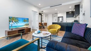 Een moderne woonkamer met een flatscreen televisie, een bank, een gele fauteuil en een eethoek.