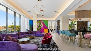 Een moderne hotelentree met een ruime zithoek, een bar en een kleurrijk muurschilderij.