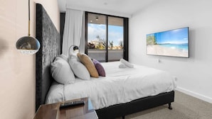 Een moderne slaapkamer met een groot bed, uitzicht op het strand door een schuifdeur, en een schilderij van een strandlandschap aan de muur.