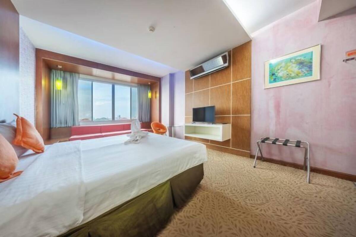 A hotel room with a bed, a TV, a small table, and a window with curtains.