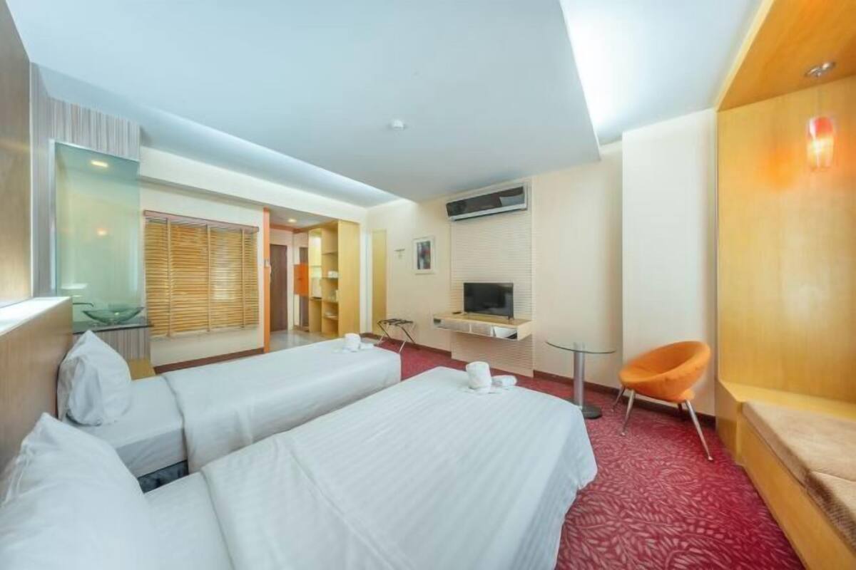 A hotel room with two beds, a TV, a desk, a chair, and a bathroom with a shower and toilet.