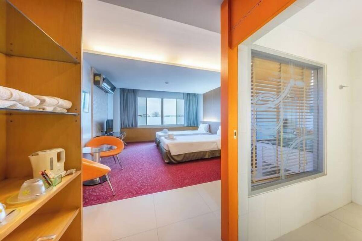 A hotel room with a bed, a desk with a chair, a window with blinds, and a staircase visible through the window.