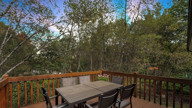 Une terrasse en bois avec une table et des chaises, entourée d’arbres et dotée d’une rambarde en bois.