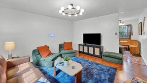 Un salon moderne avec un téléviseur à écran plat, des canapés verts, une table basse et un tapis bleu.