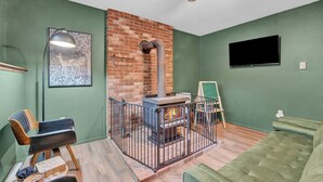 Une pièce avec une cheminée en briques, un canapé vert, une chaise en bois et un téléviseur à écran plat fixé au mur.