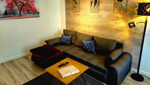 Una sala de estar moderna con un sofá, dos almohadas, una manta roja, un control remoto y una revista sobre una mesa de centro de madera.