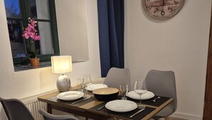 Un comedor con una mesa preparada para cuatro, sillas, un reloj y una ventana con cortinas.