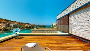 A wooden deck with a lounge chair and a flower vase, overlooking a coastal town and a clear blue sea. - Villa Flora Mare IV with Two Pools (Primošten)