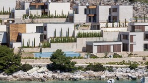 A coastal residential area with modern architecture, featuring multi-story buildings with balconies, a rocky shoreline, and boats in the water. - Villa Flora Mare IV with Two Pools (Primošten)