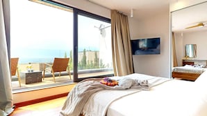 Habitación de hotel con una cama grande, televisión, balcón con una silla y vista al mar.