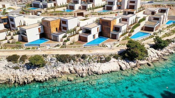 Un complejo turístico costero con villas modernas, piscinas y terreno rocoso.