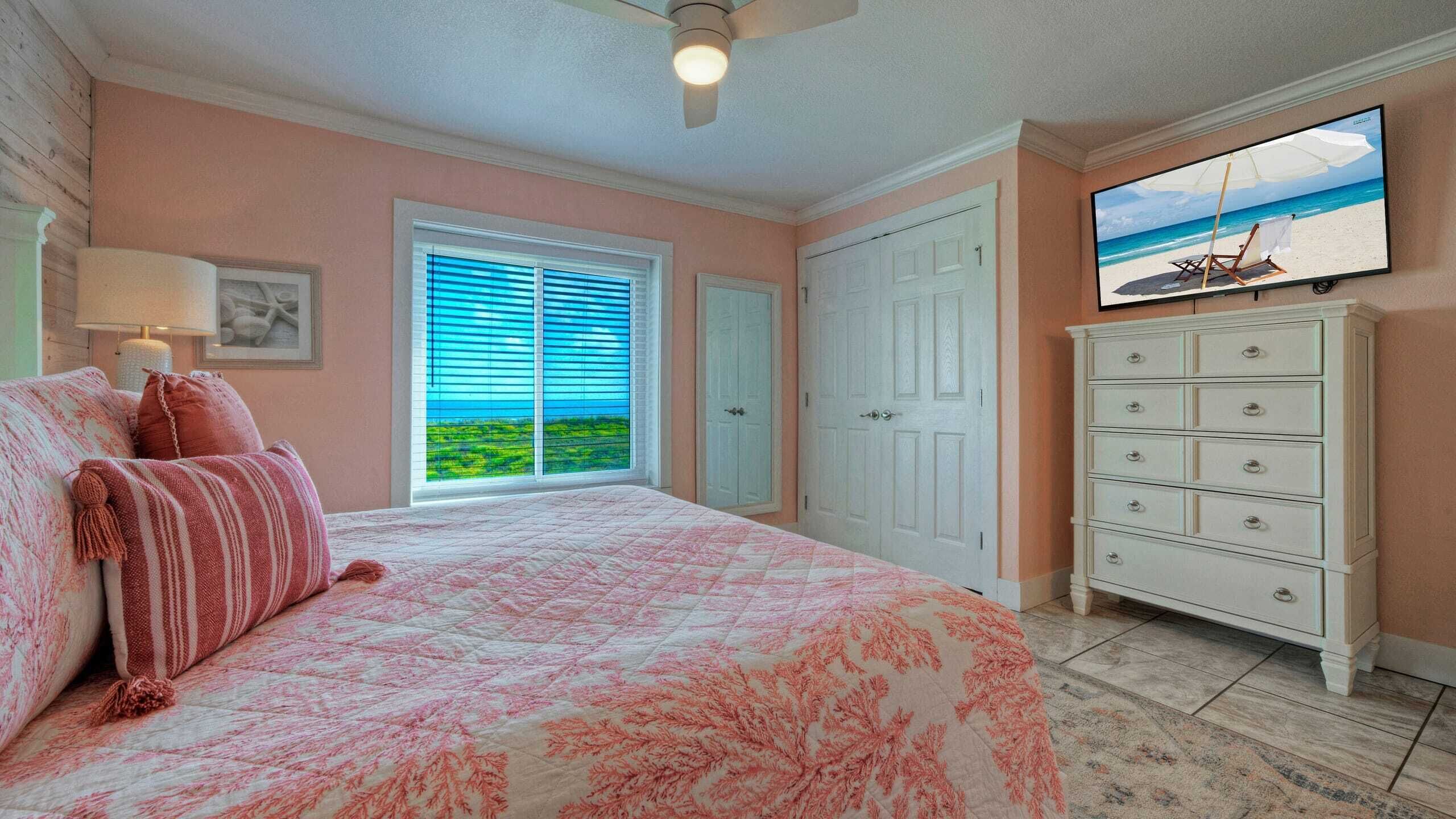 A bedroom with a bed, a dresser, a TV, and a window with a view of the ocean.