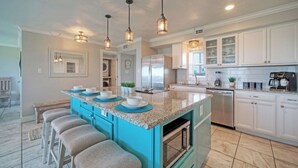 A kitchen with a central island, bar stools, a refrigerator, a dishwasher, and a coffee maker. - Gulf Views + Pools, Tennis, Pickleball & Beach Access Awesome Beachfront by Avantstay (Port Aransas)