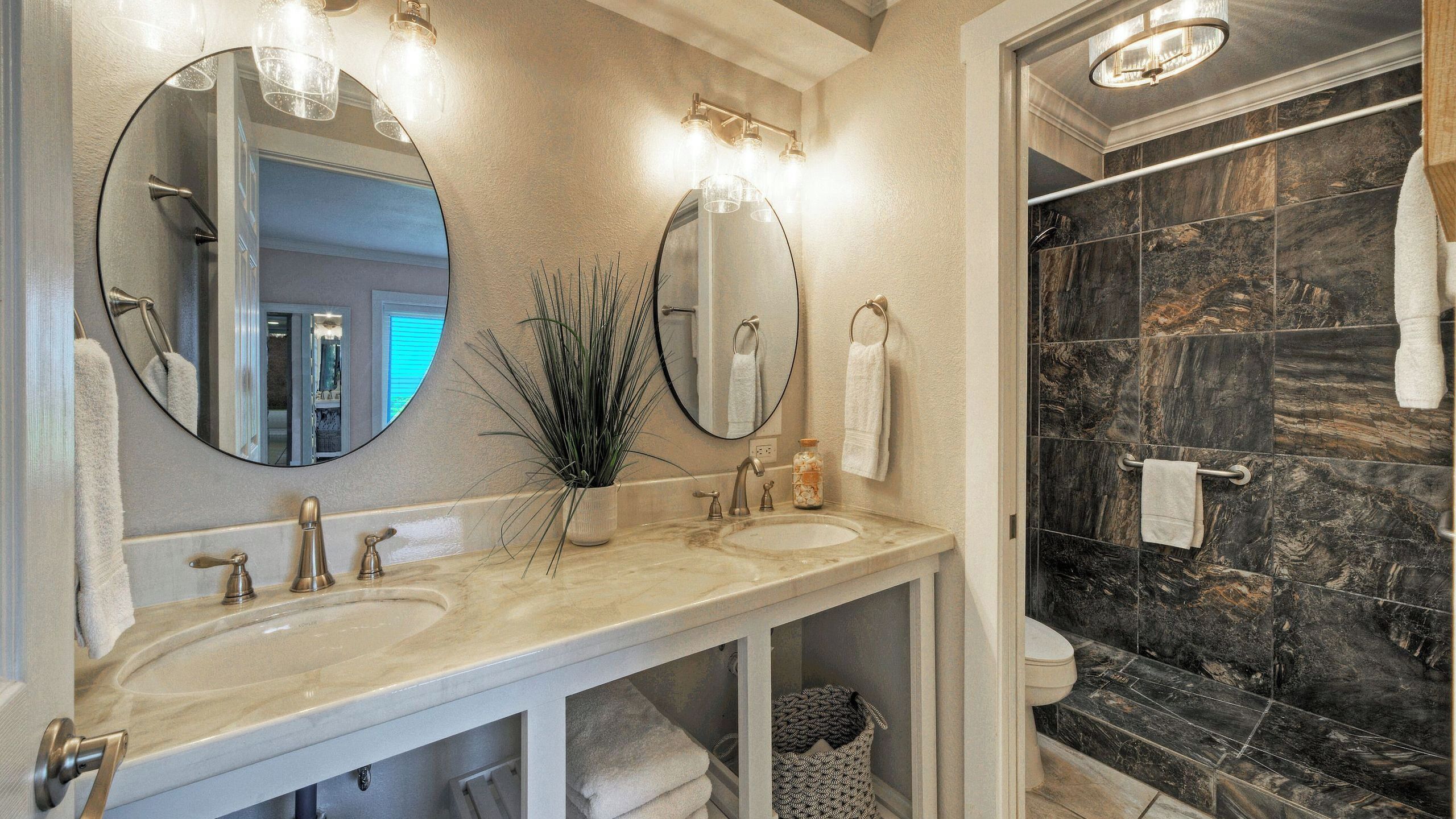 A bathroom with two sinks, a large mirror, and a shower with dark tiles.