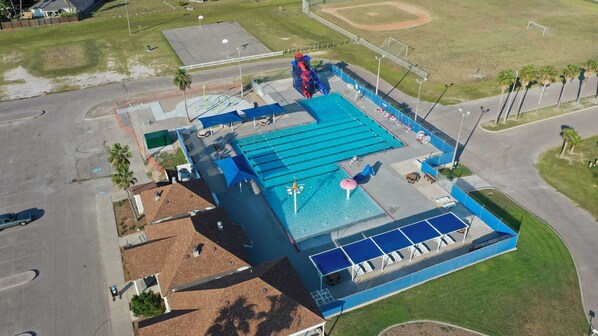 A large swimming pool with a blue deck, surrounded by a fenced area with palm trees.