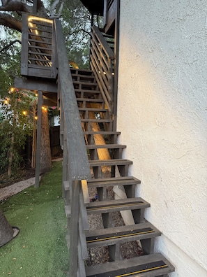 A wooden staircase with a handrail, leading to a wooden platform with string lights.