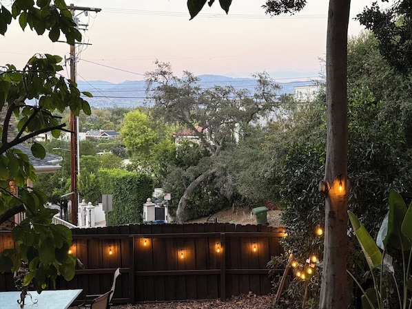 A backyard with a wooden fence, string lights, and a view of a residential area with houses and trees.